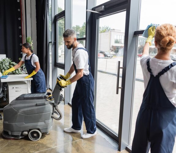 man with electrical floor scrubber machine near interracial women cleaning office,stock image